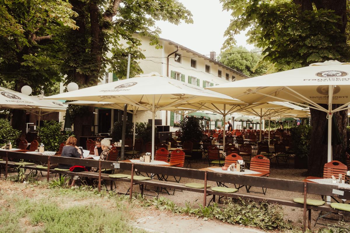 Biergarten der Emmeramsmühle vor der historischen Fassade mit grünen Fensterläden und blühenden Geranien