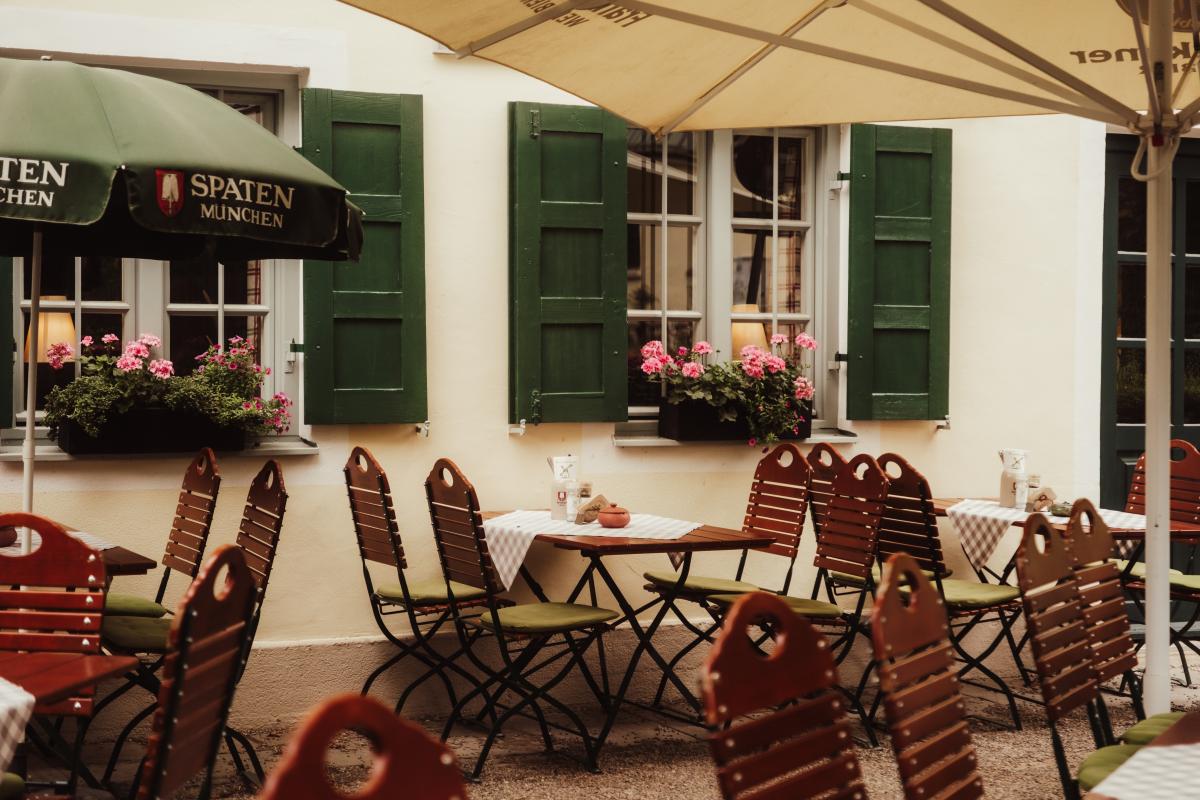 Gemütliche Sitzplätze im Biergarten der Emmeramsmühle entlang des historischen Gebäudes mit grünen Fensterläden