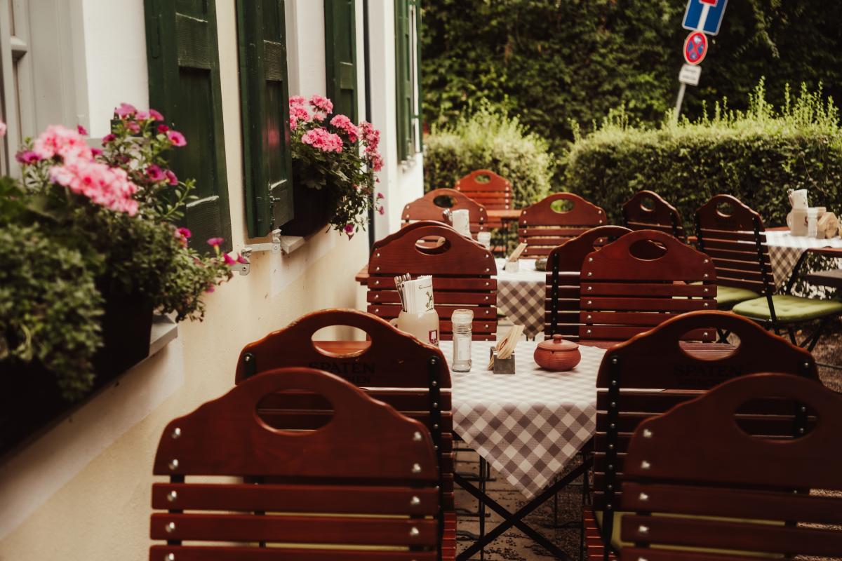 Idyllischer Sitzplatz im Biergarten der Emmeramsmühle vor einem Fenster mit grünen Fensterläden und Blumen