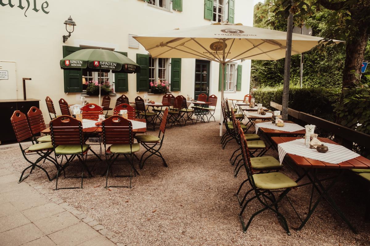 Biergarten der Emmeramsmühle mit traditionellen Biergartenstühlen, gedeckten Tischen und großen Sonnenschirmen