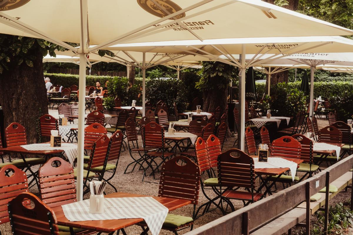 Großzügiger Biergarten der Emmeramsmühle mit gedeckten Tischen unter Sonnenschirmen und schattenspendenden Bäumen