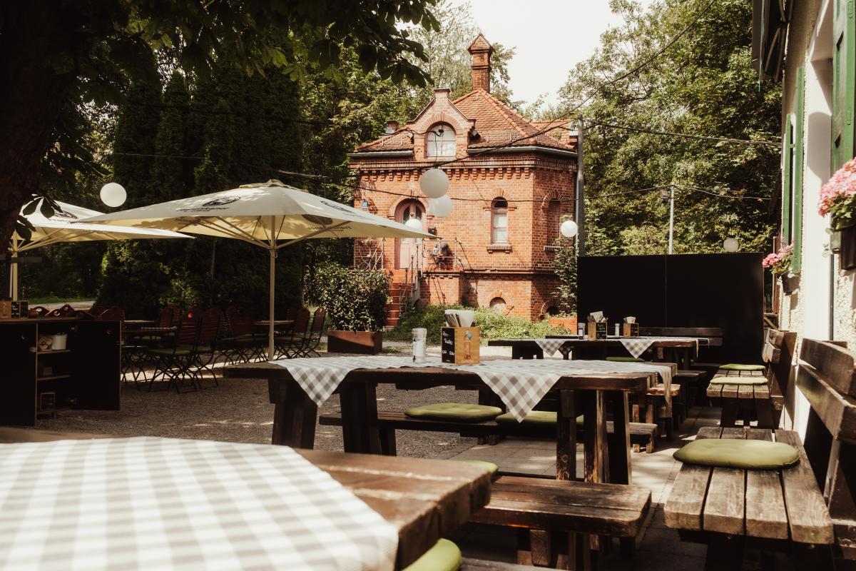 Gemütlicher Biergarten der Emmeramsmühle mit Holztischen und Blick auf das historische Backsteingebäude