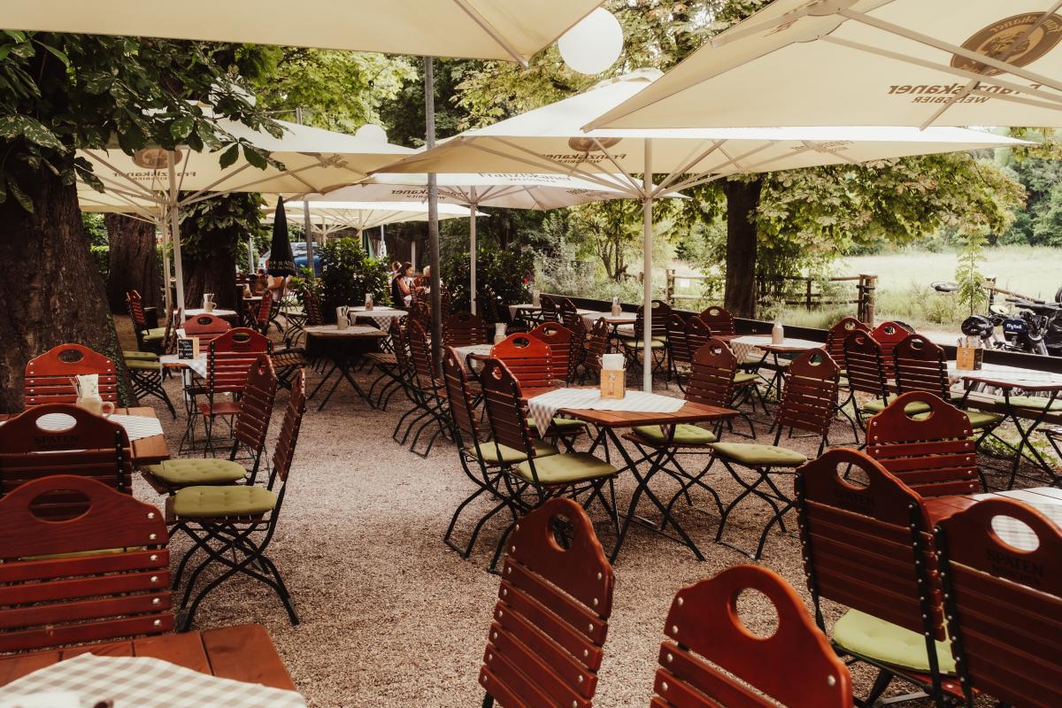Schattiger Biergarten der Emmeramsmühle mit gedeckten Tischen unter Sonnenschirmen und Blick ins Grüne