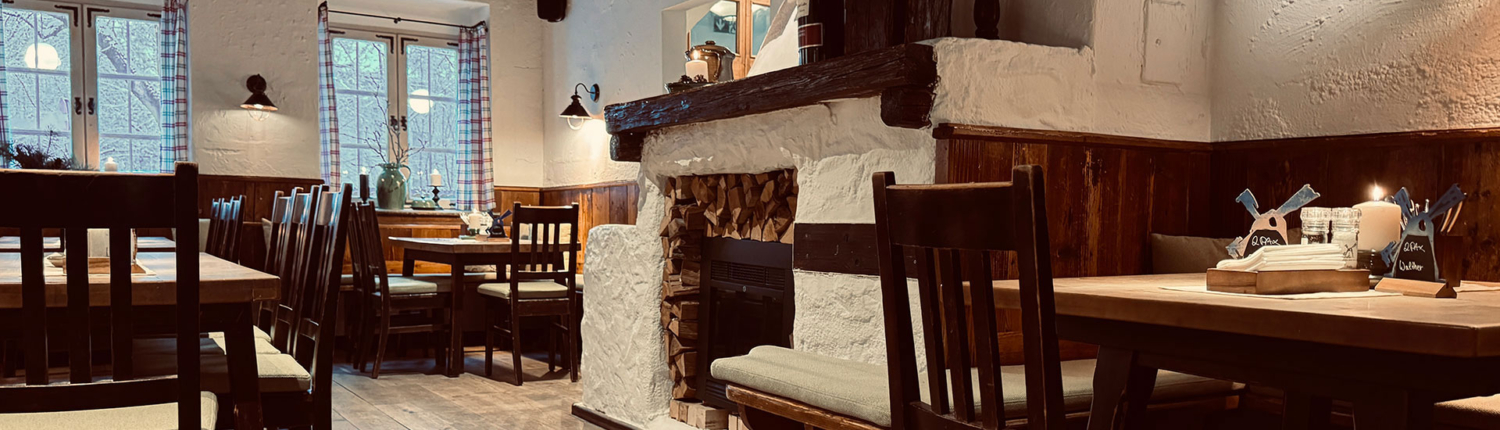 Gemütlicher Gastraum der Emmeramsmühle mit Holztischen, Sitzbänken und Kamin
